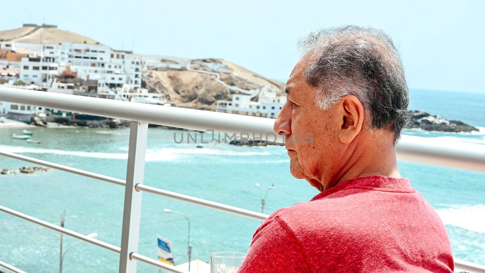 Mature man sitting on a balcony overlooking the sea with a cocktail