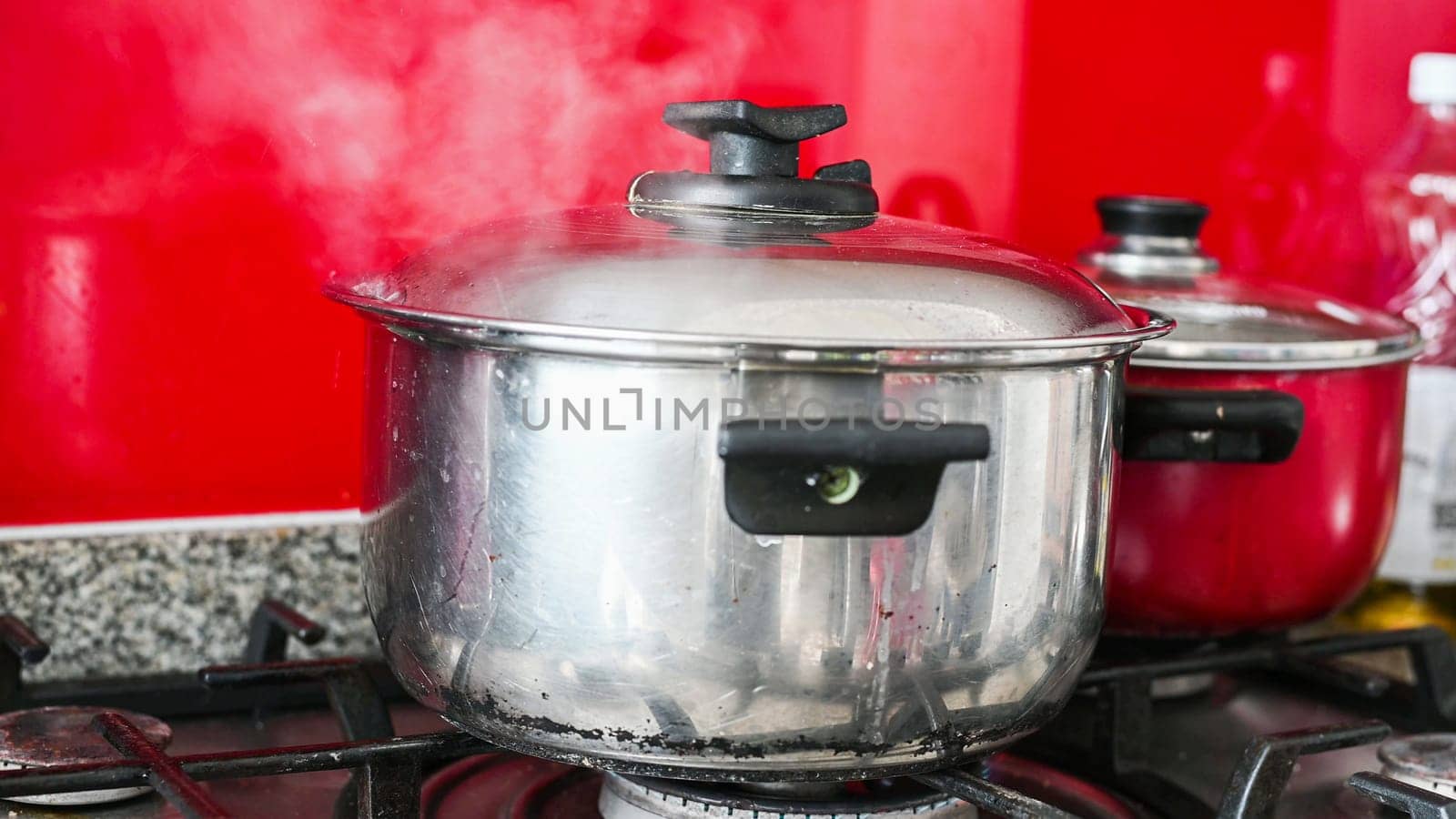 Steam or Vapour clouds rising from boiling water in saucepan on stove. Steam from pan while cooking