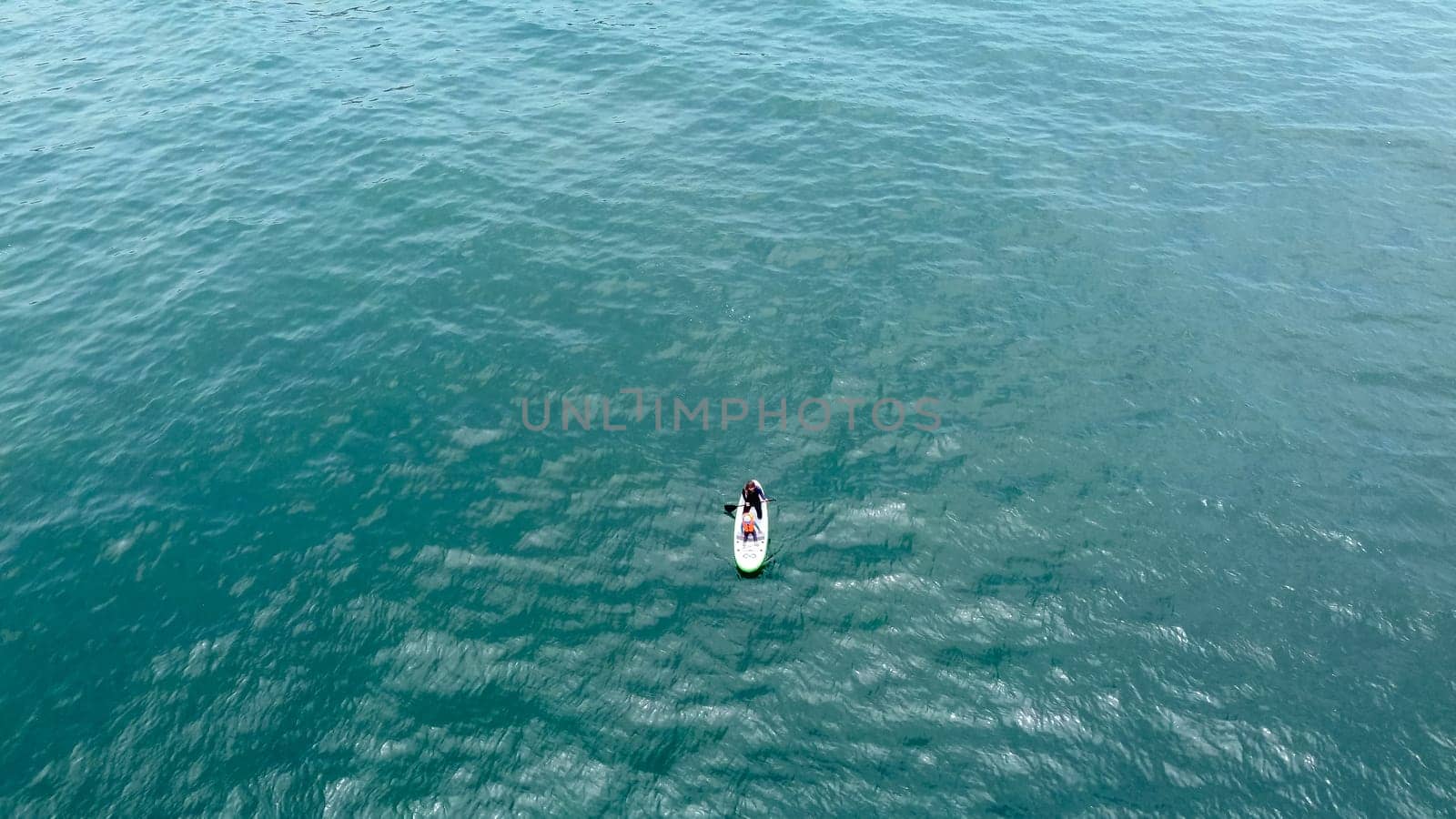 Aerial shot. Young woman and baby have fun paddling in the sea on a board. by Peruphotoart