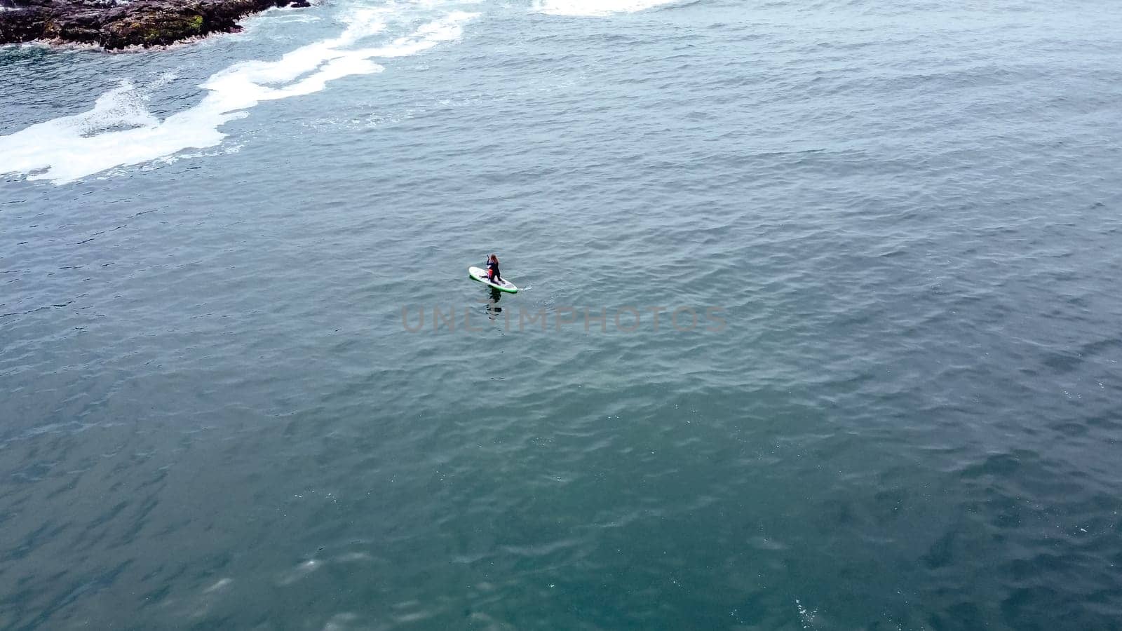 Aerial shot. Young woman and baby have fun paddling in the sea on a board