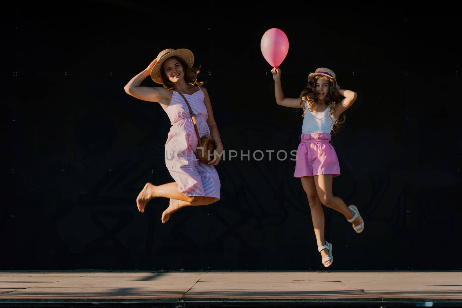 mother and daughter jumping in pink dresses with loose long hair on a black background. Enjoy communicating with each other by Matiunina