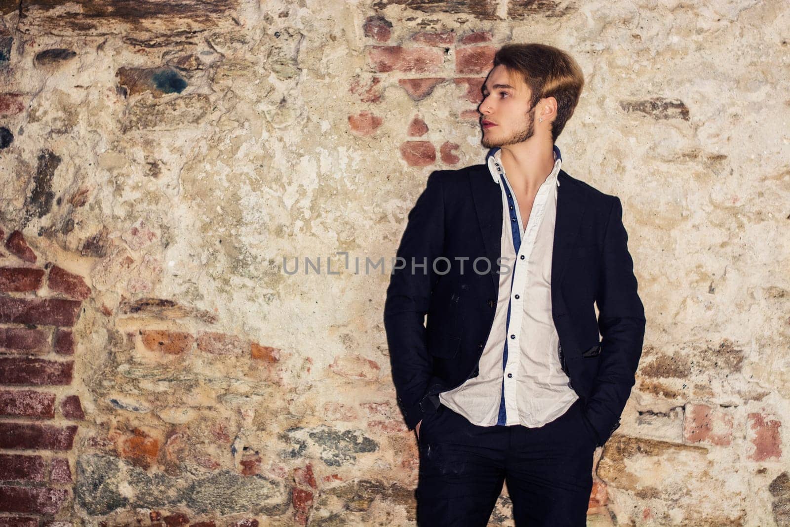 Handsome blond young man standing against brick wall, looking away to a side, wearing white shirt and jacket