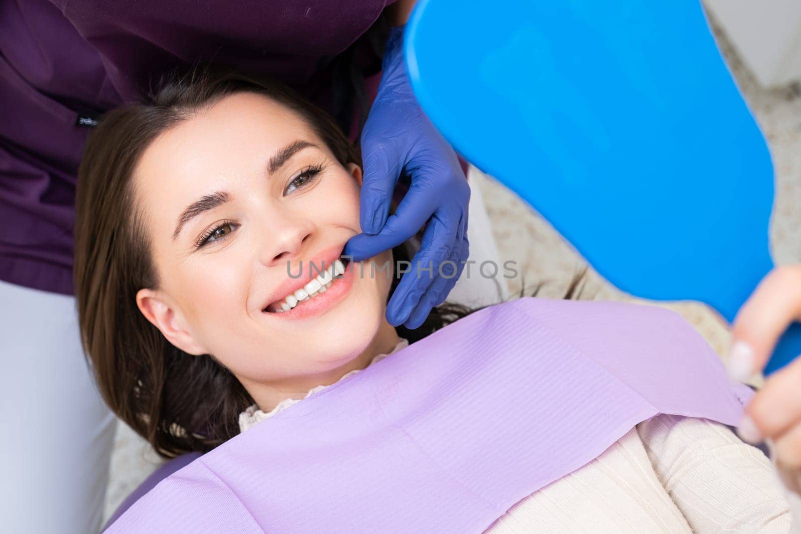 Dentist demonstrates the result of teeth treatment or professional dental cleaning, while happy patient looks in the mirror