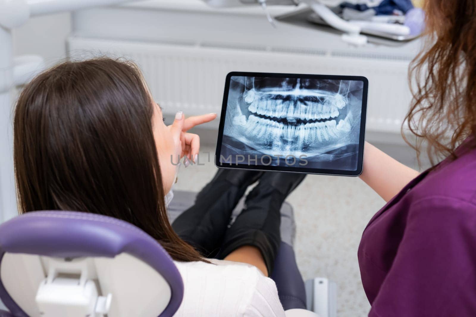 Dentist converses with the patient about treatment strategies while using a tablet to display the X ray image.
