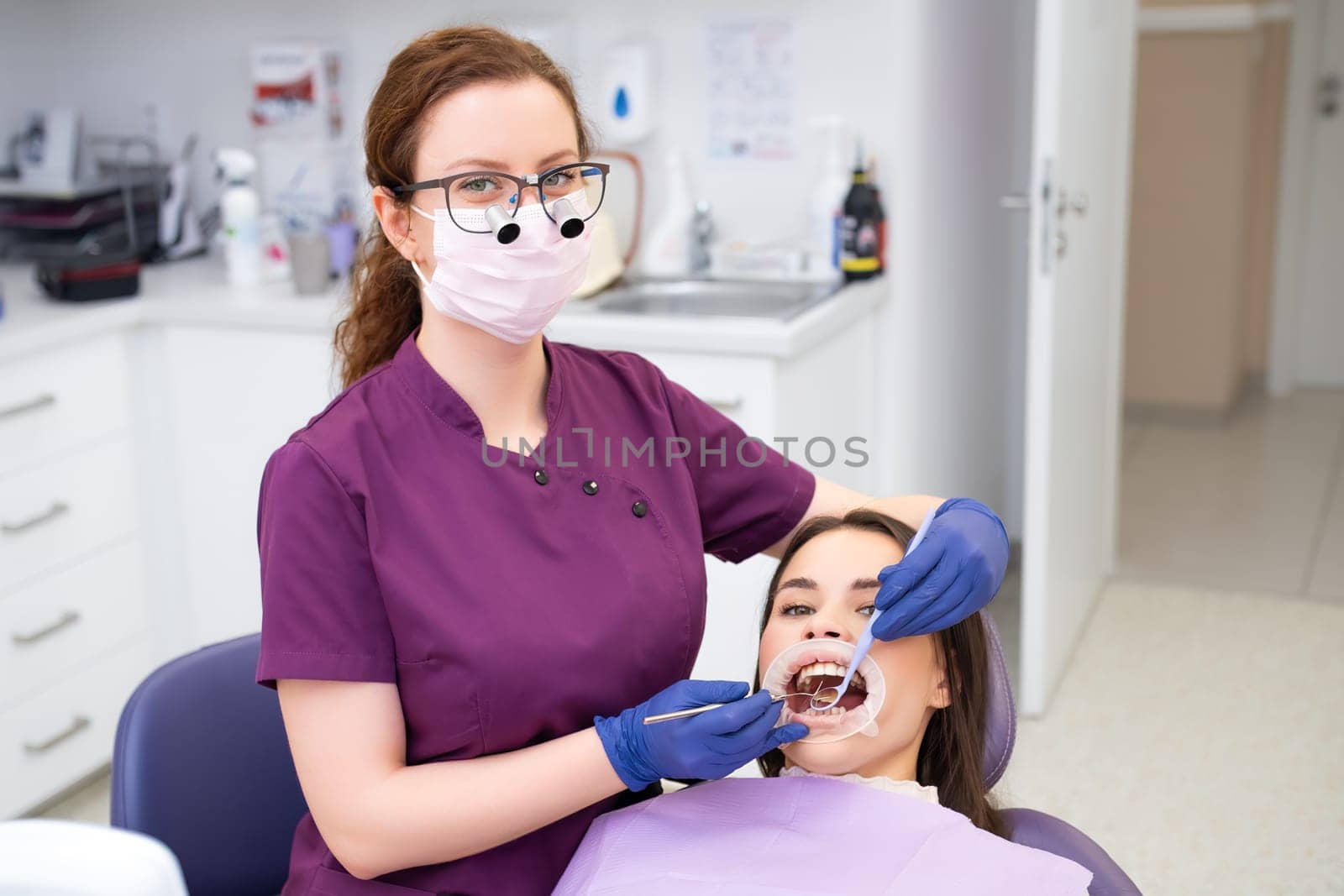 Portrait of female dentist examing teeth of the young beautiful patient.