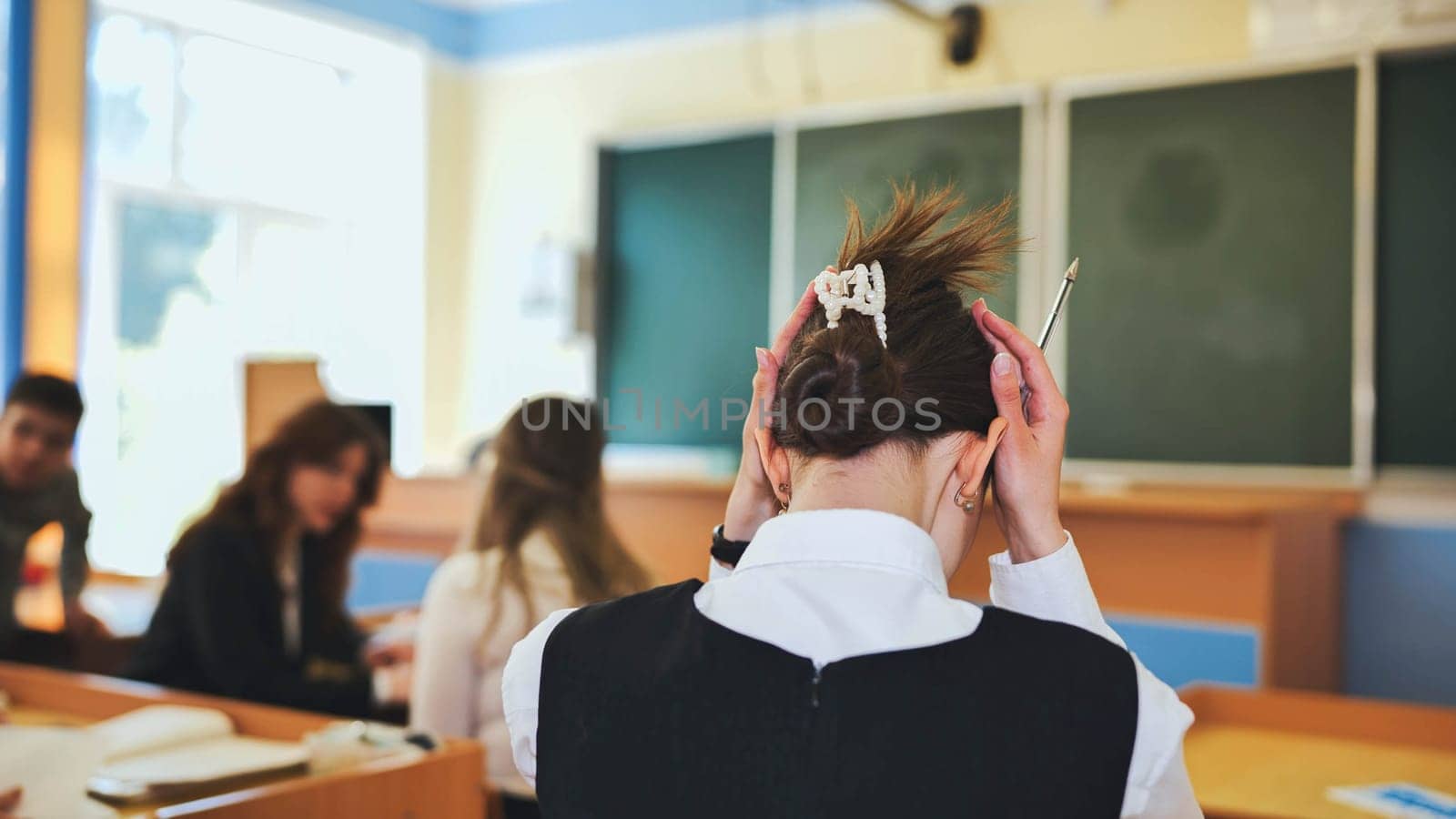 A schoolgirl fixes her hair during class. by DovidPro
