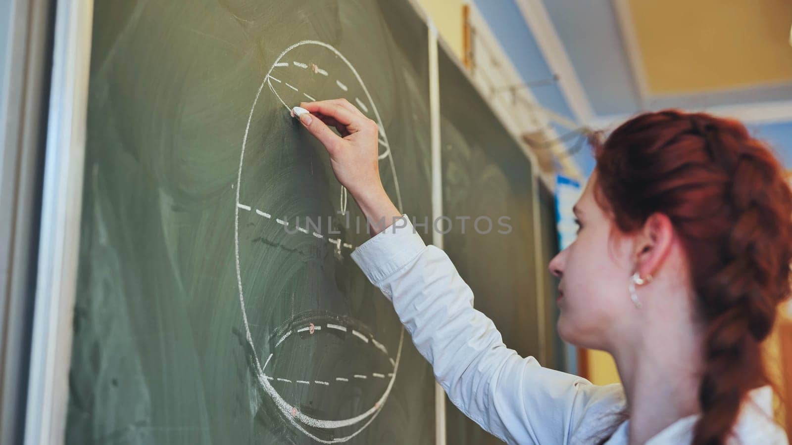 A red-haired schoolgirl draws geometric shapes on the blackboard