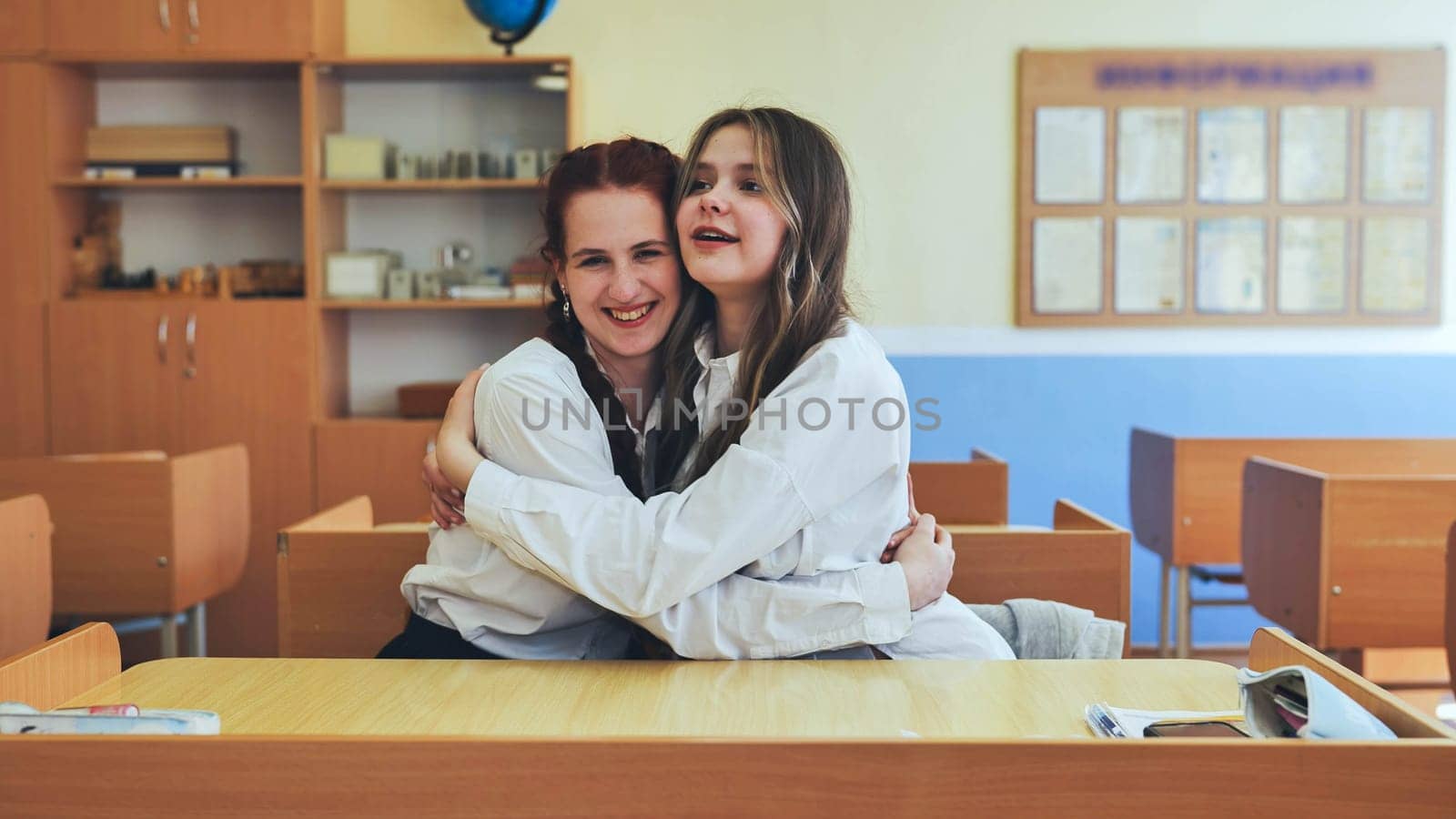 Girl students hugging in a classroom at school. Translate: Information. by DovidPro