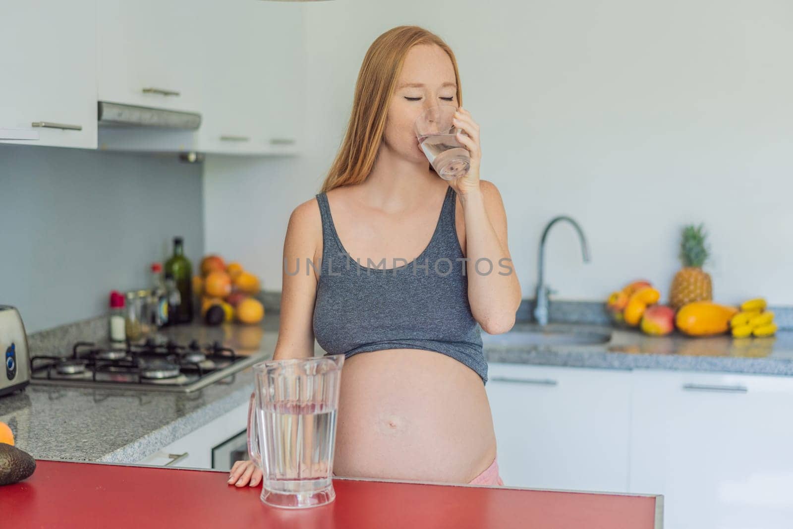 Embracing the vital benefits of water during pregnancy, a pregnant woman stands in the kitchen with a glass, highlighting hydration's crucial role in maternal well-being by galitskaya