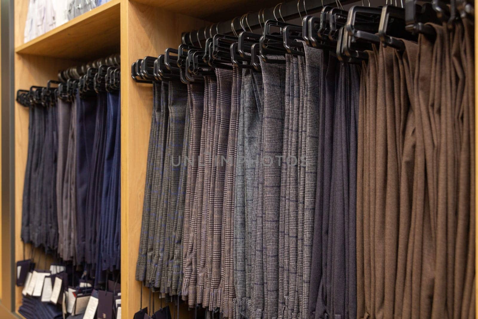 Men's classic trousers on hangers in a boutique. Showcase with many men's trousers hanging on hangers in stock on hangers in a men's clothing store.