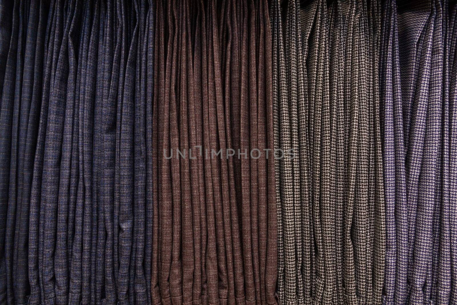 Background with men's classic trousers on hangers in a boutique. Showcase with many men's trousers hanging on hangers in stock on hangers in a men's clothing store.