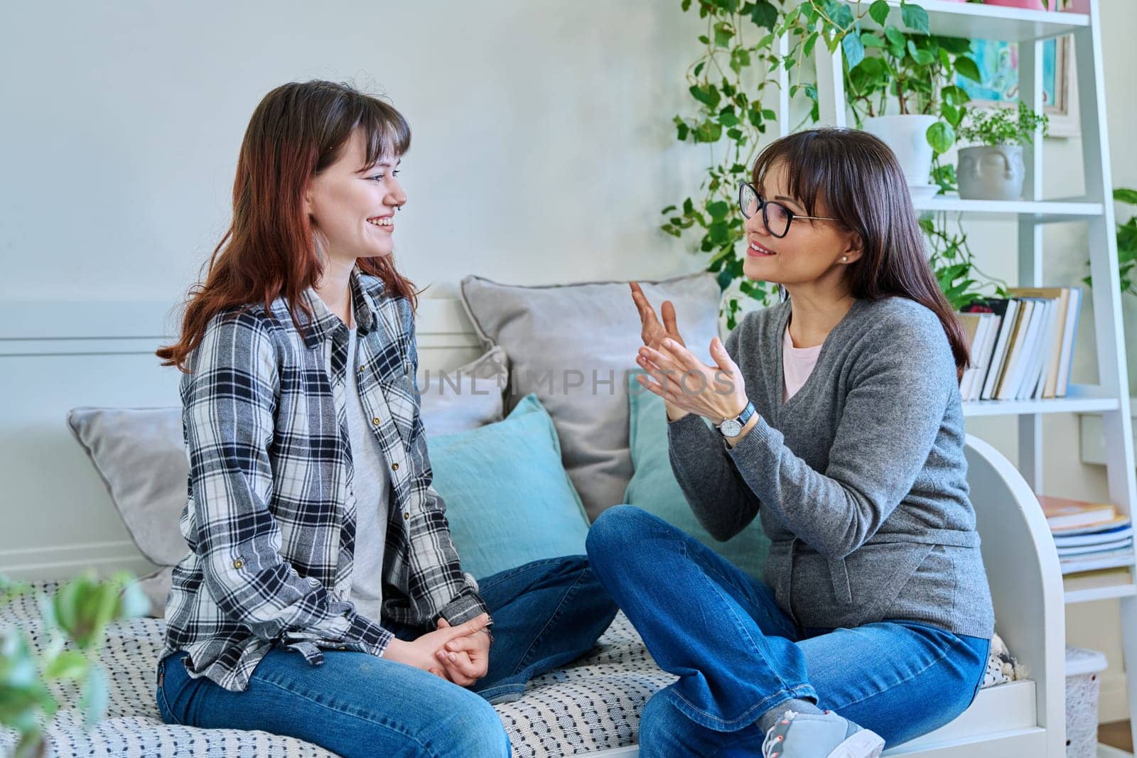 Talking mother and teenage daughter sitting together on couch at home by VH-studio