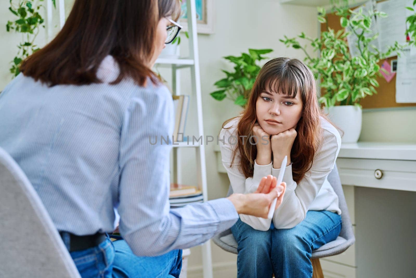 Sad, serious teenage girl at session in office of mental professional by VH-studio