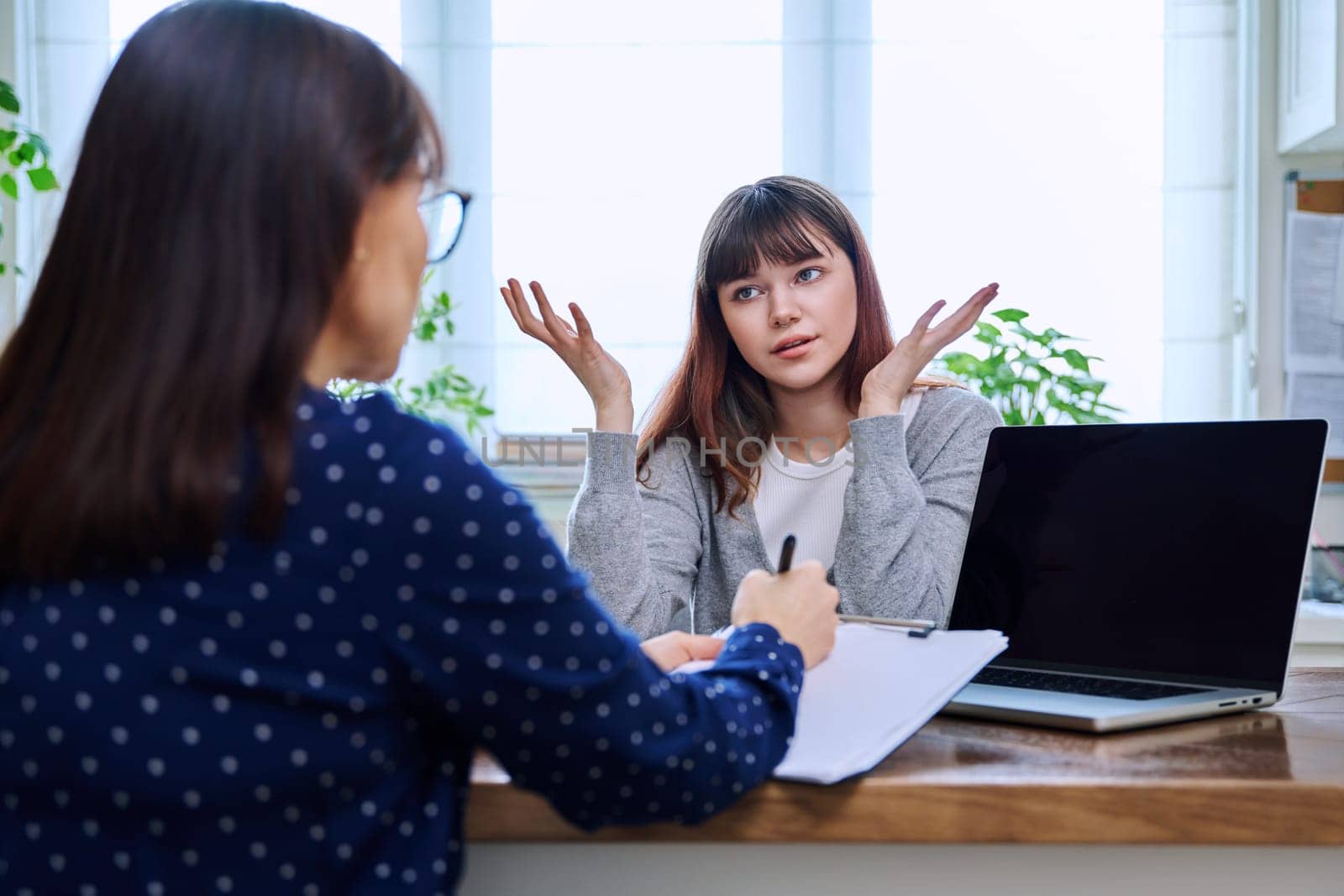 Teenage girl college student at therapy meeting with mental health professional social worker psychologist counselor sitting together in office. Psychology, psychotherapy, mental assistance support
