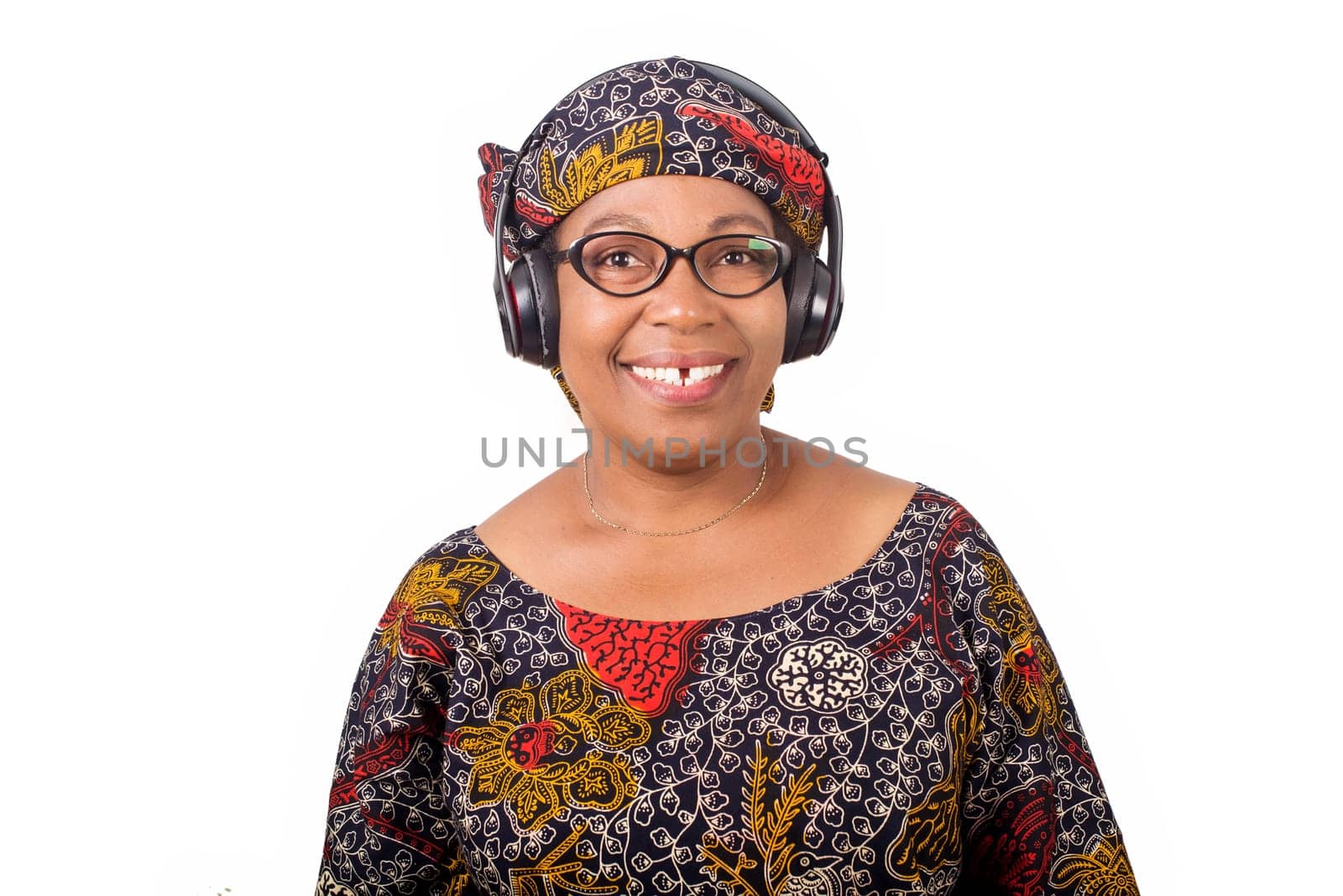 smiling mature african woman in african loincloth and scarf listening music with headphones on white background