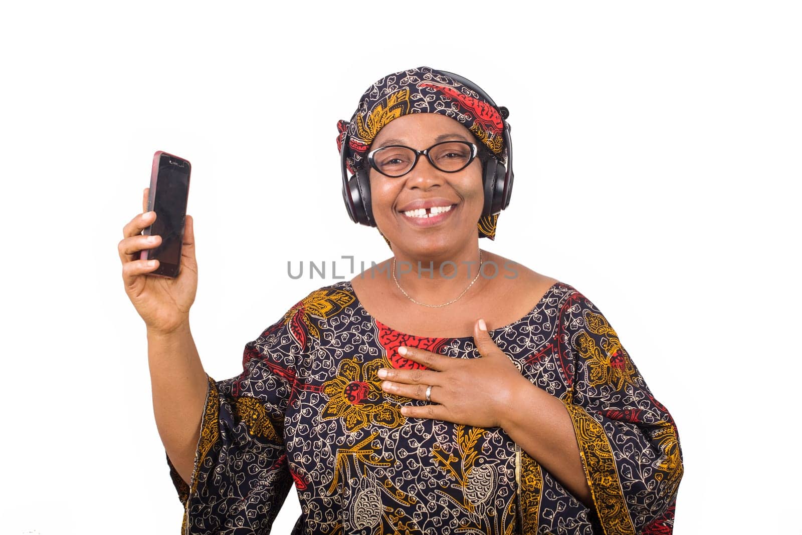 mature african woman in loincloth listening music using headphones and cellphone having hand gesture