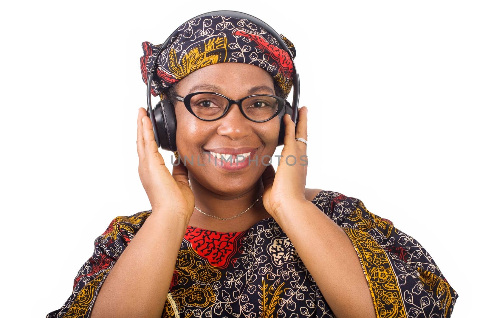 smiling mature african woman in african loincloth and scarf listening music with headphones on white background