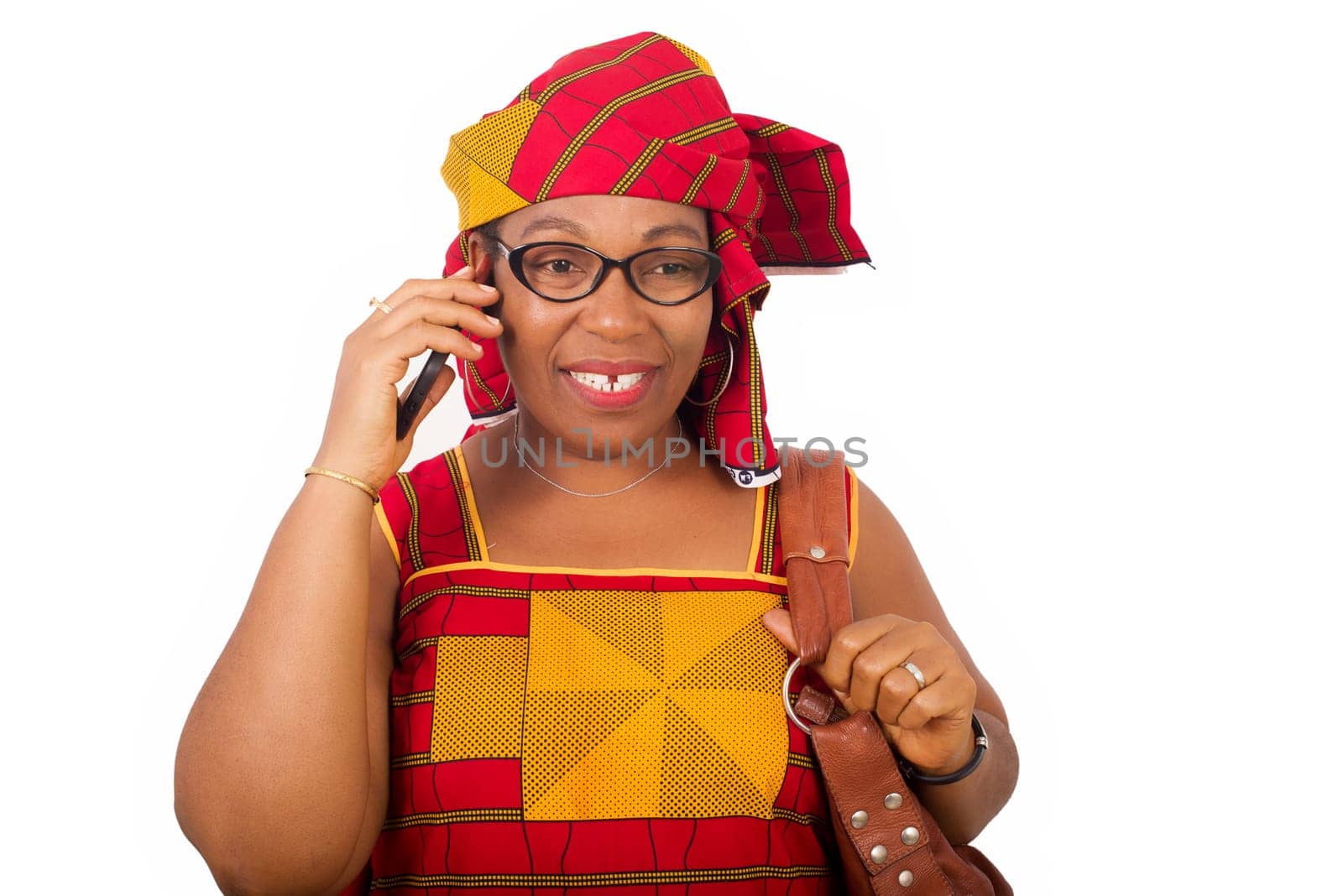 mature woman in red african outfit with glasses, talking on smart phone with smile. Smiling woman with a mobile phone in her hand. Mobile communication, isolated on white background.