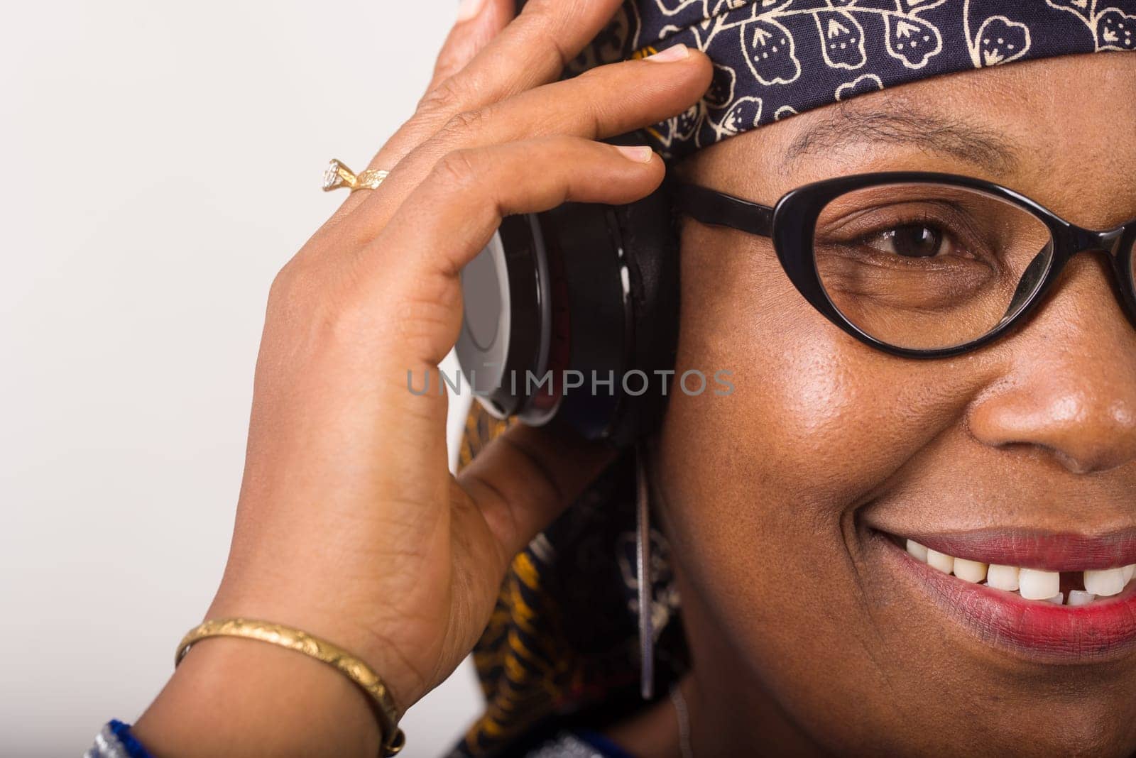 mature woman standing on white background listening to music using headphones while smiling.