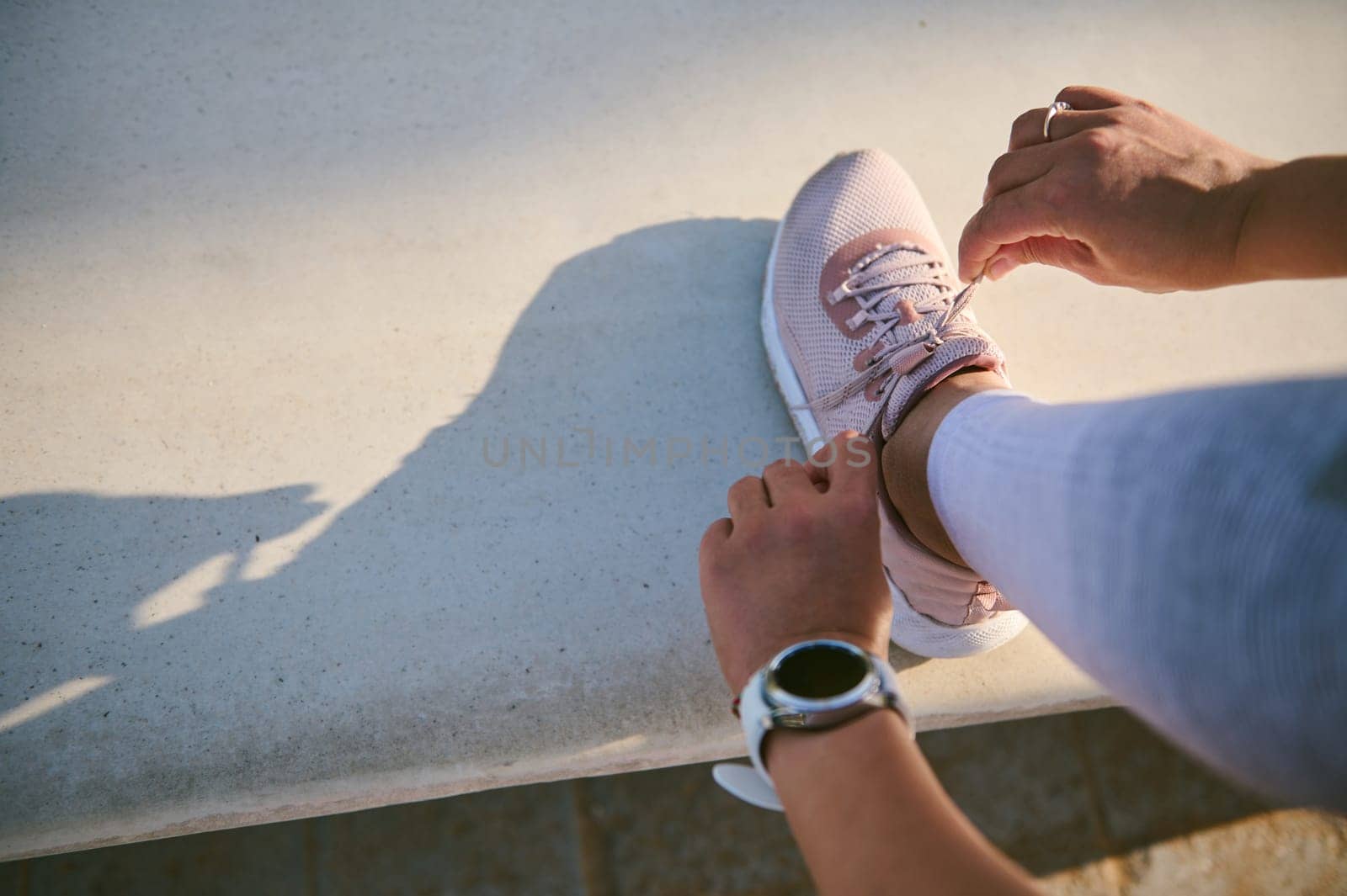 Top view female athlete, sportswoman tying laces on pink sneakers, wearing smart wristwatch on hand for checking and pulse control, heart rate and loosed calories, ready for morning run or workout