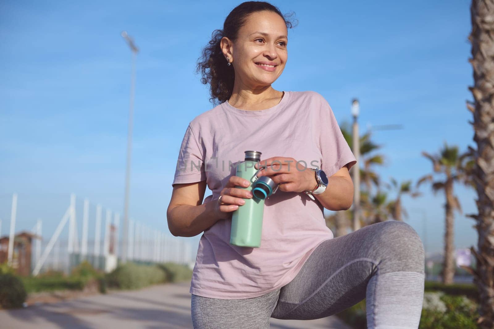 Smiling happy female athlete, determined sportswoman drinking water after playing sports on the beach by artgf