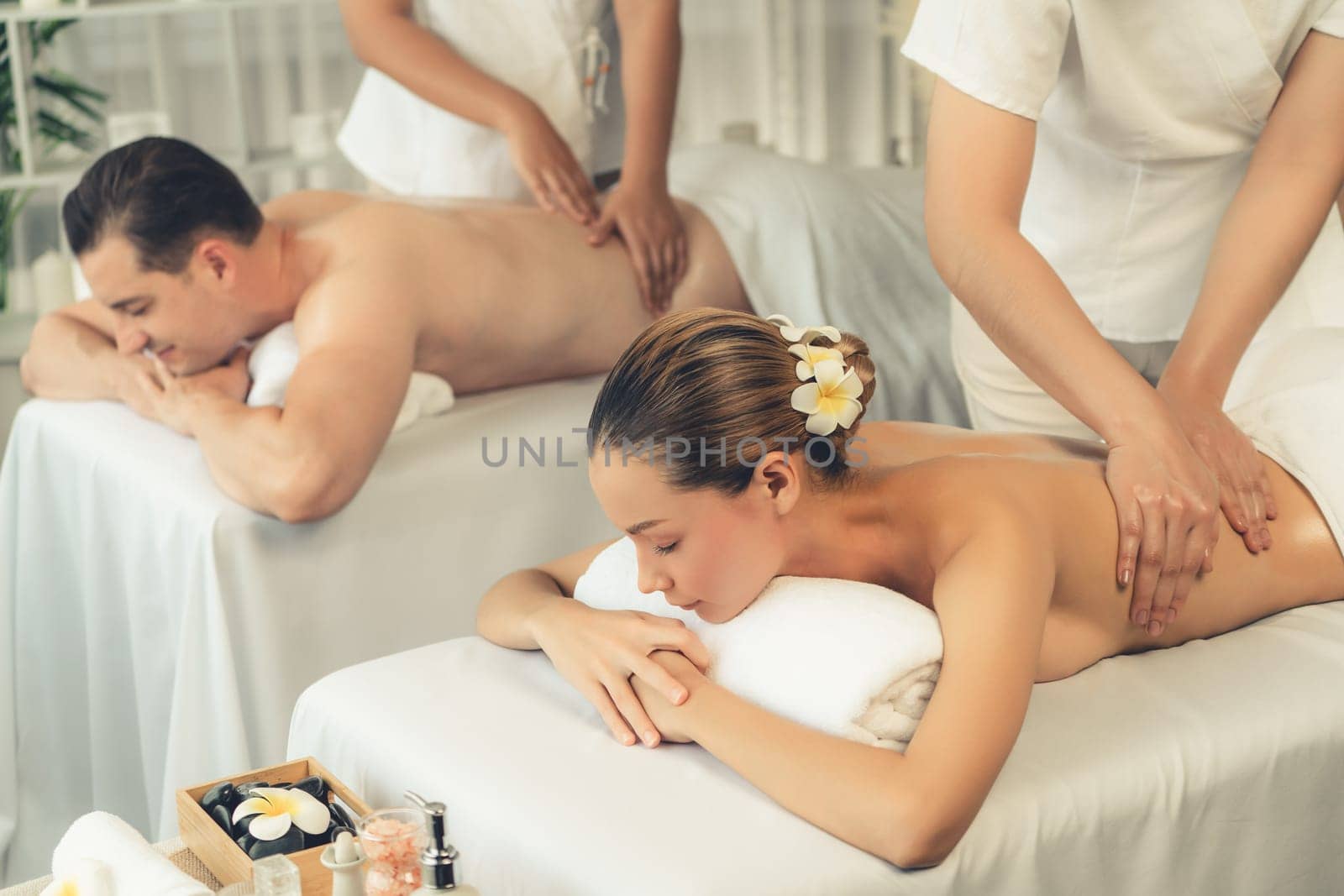 Caucasian couple customer enjoying relaxing anti-stress spa massage and pampering with beauty skin recreation leisure in day light ambient salon spa at luxury resort or hotel. Quiescent