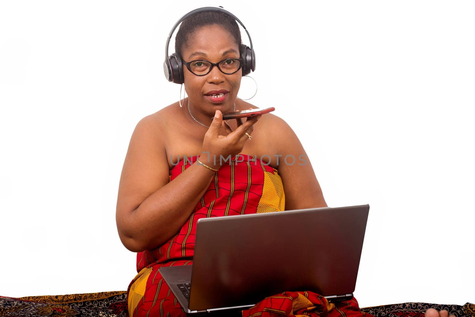 mature woman in loincloth sitting on white background with laptop computer communicating on cellphone.