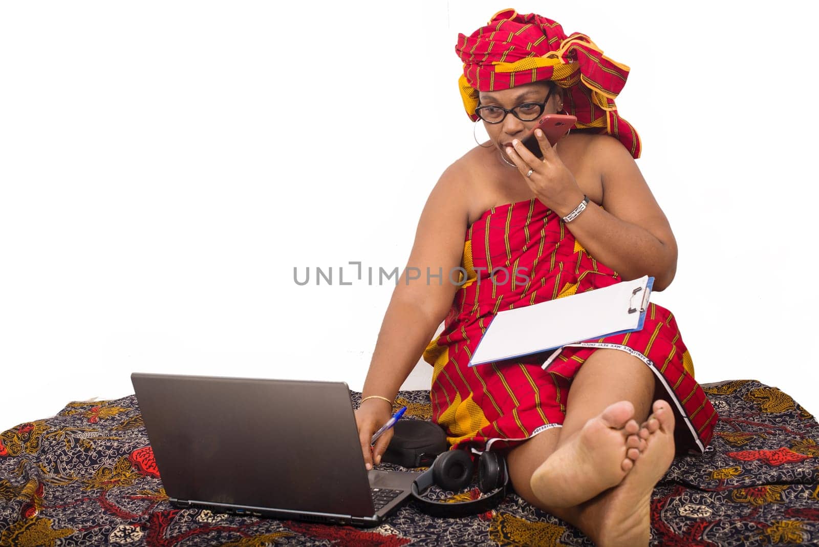 mature woman in loincloth sitting on the floor talking on mobile phone looking at laptop.