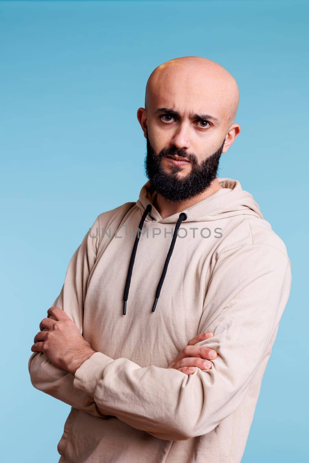 Serious arab man frowning eyebrows while posing with crossed arms studio portrait. Confused person with tensed facial expression standing with folded hands and looking at camera