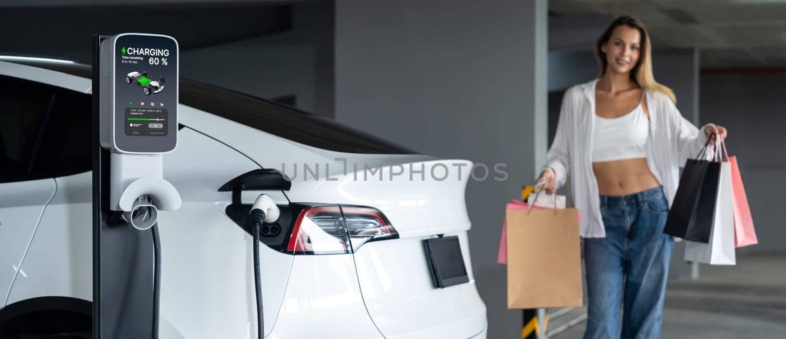 Young woman travel with EV electric car to shopping center parking lot innards by biancoblue