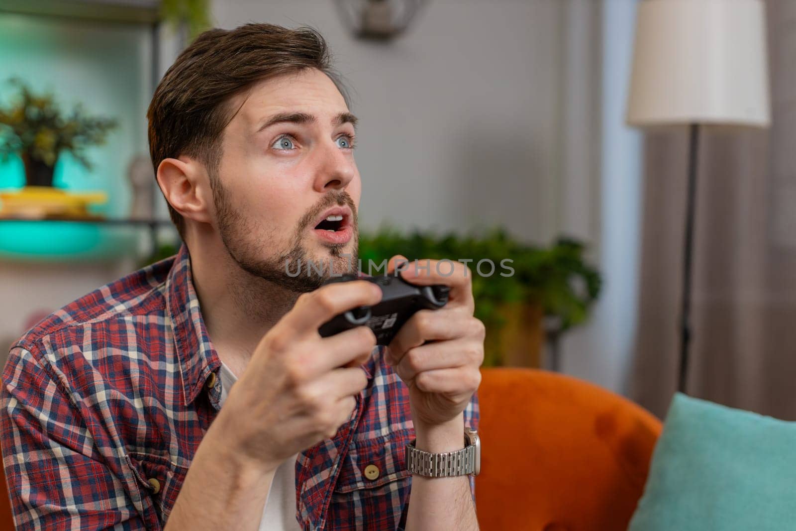 Close-up young man using joystick controller playing video console television game fun enjoying sits on couch in living room. Caucasian guy enjoying success winning online game during weekend at home
