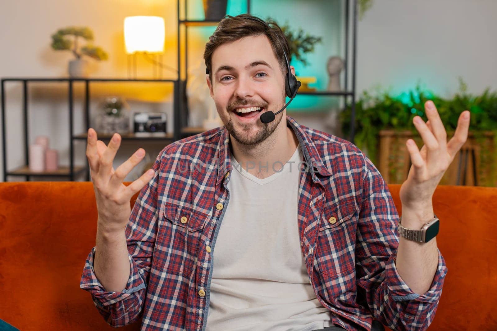 Call me. Happy Caucasian man sitting on sofa at home wearing headset, freelance worker, call center, support service operator helpline, having talk with client or colleague, communication support