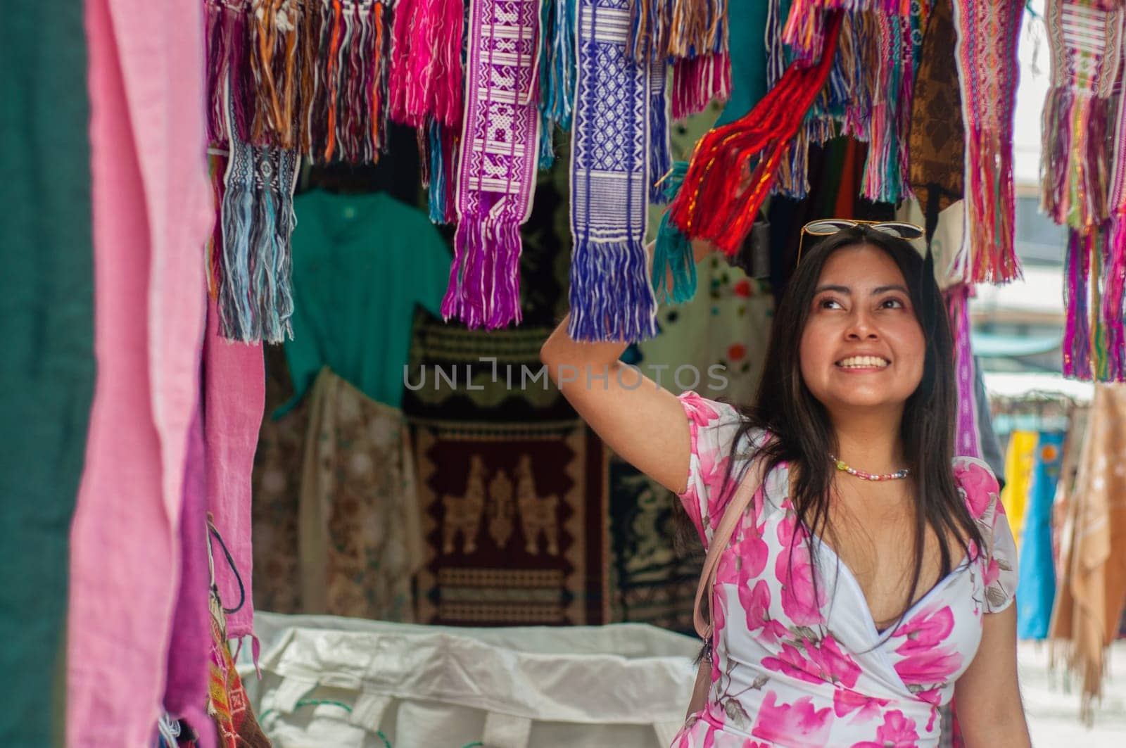 A cheerful woman goes sightseeing and chooses a brightly colored scarf from an assortment of handcrafted fabrics displayed at an open-air market stall. by Raulmartin