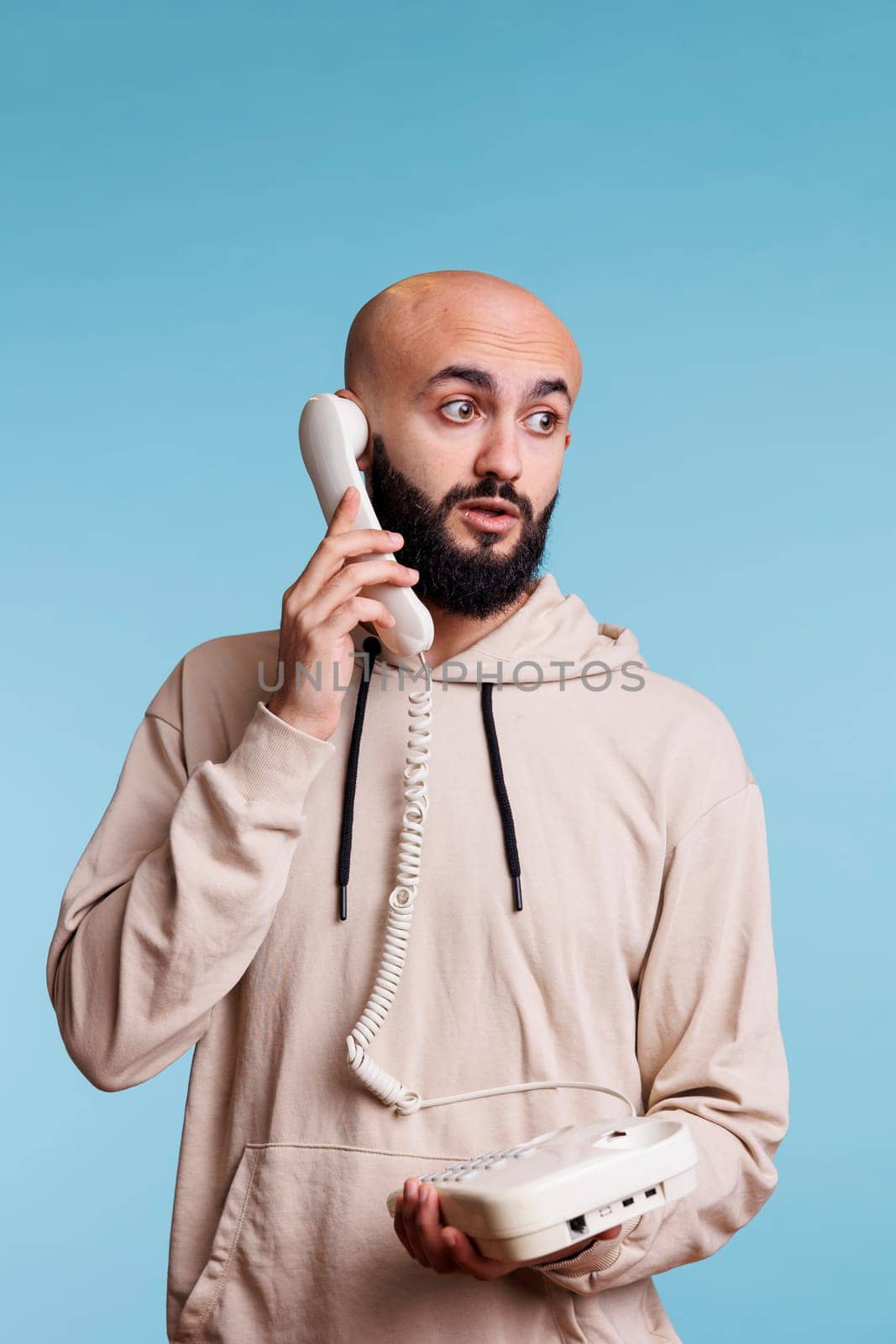 Arab man answering landline phone call and looking away with surprised expression. Young person talking on old fashioned corded telephone, having conversation, listening to interlocutor