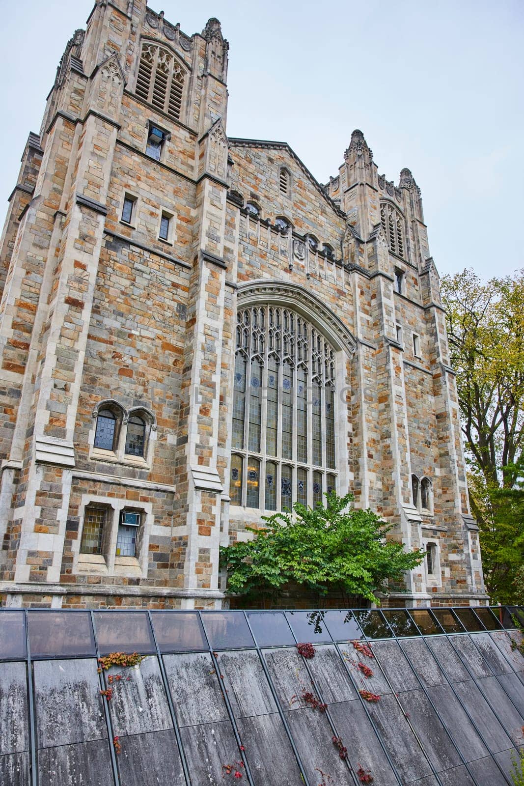 Gothic architecture of the University of Michigan Law Quadrangle, an iconic historical building amidst modern elements in Ann Arbor, under an overcast sky.