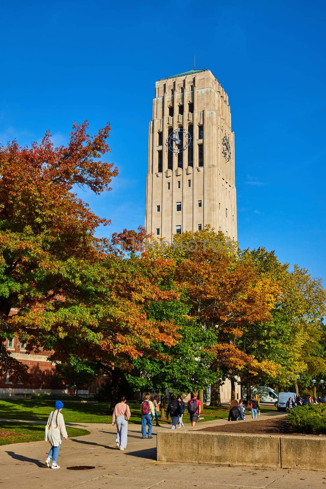 Students stroll under the historic Burton Memorial Tower amid a vibrant autumn setting at the University of Michigan, Ann Arbor, embodying the essence of college life and academia.