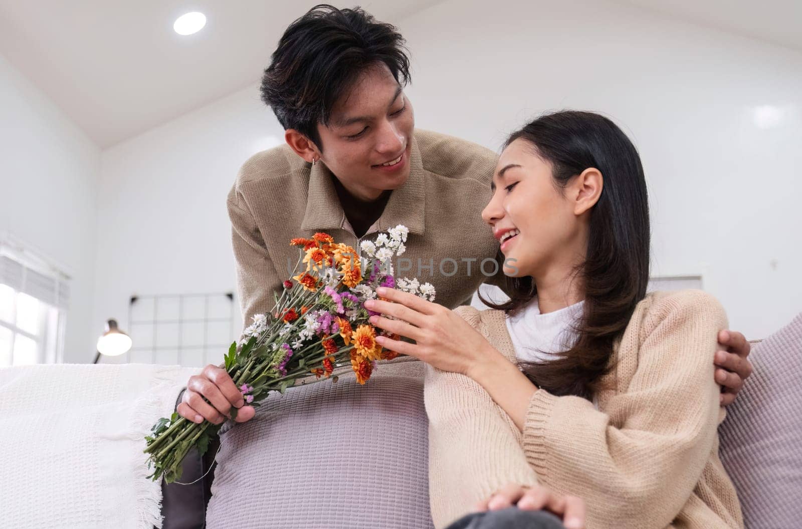 A young Asian couple gives flowers to each other on their anniversary and sits happily together in the living room..