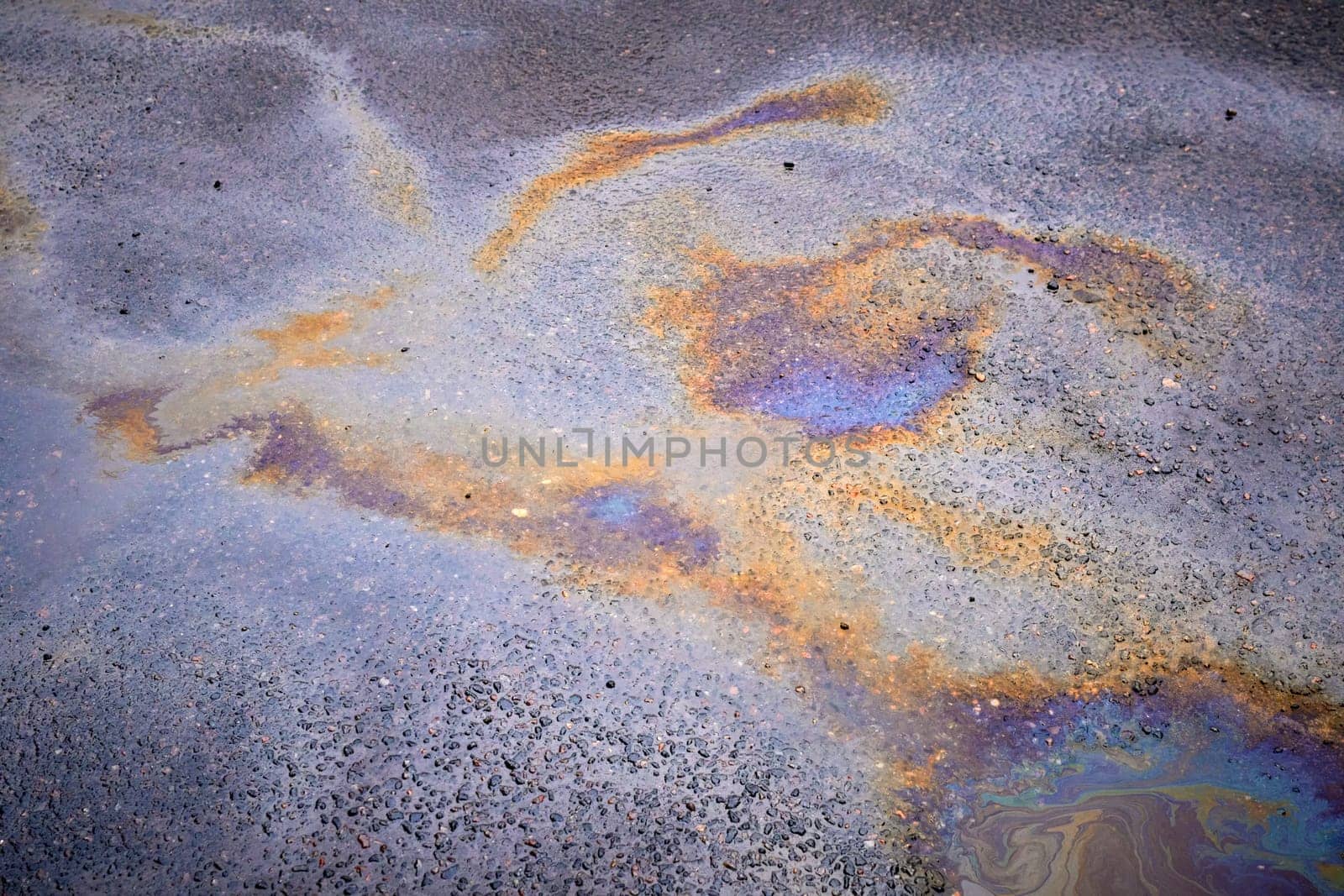 Colorful rainbow stains of an oil spill on wet asphalt.