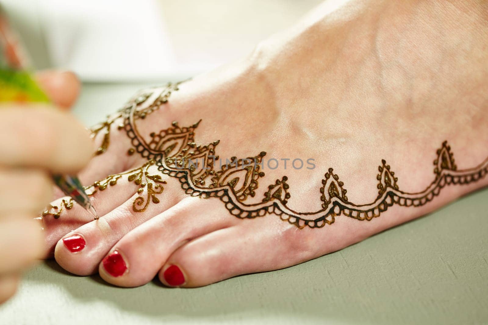 Mehendi. Master applying henna on model's leg, close-up