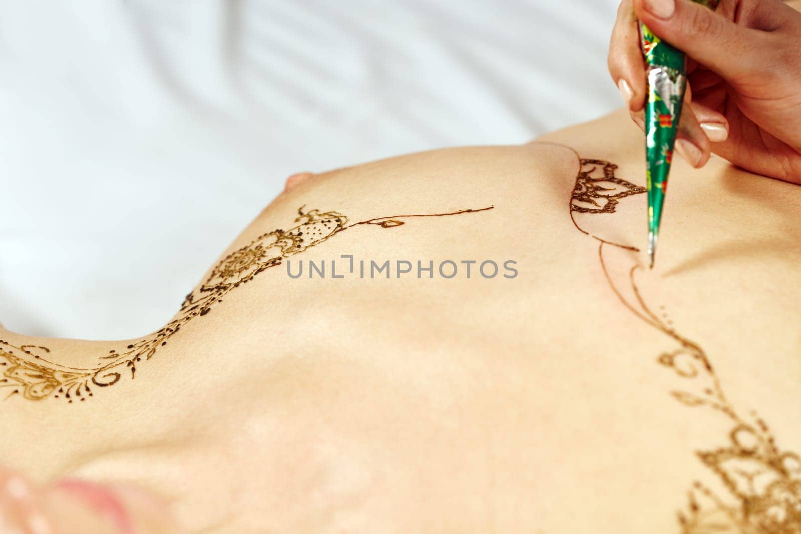 Mehndi. Master paints with henna on bare model's breasts