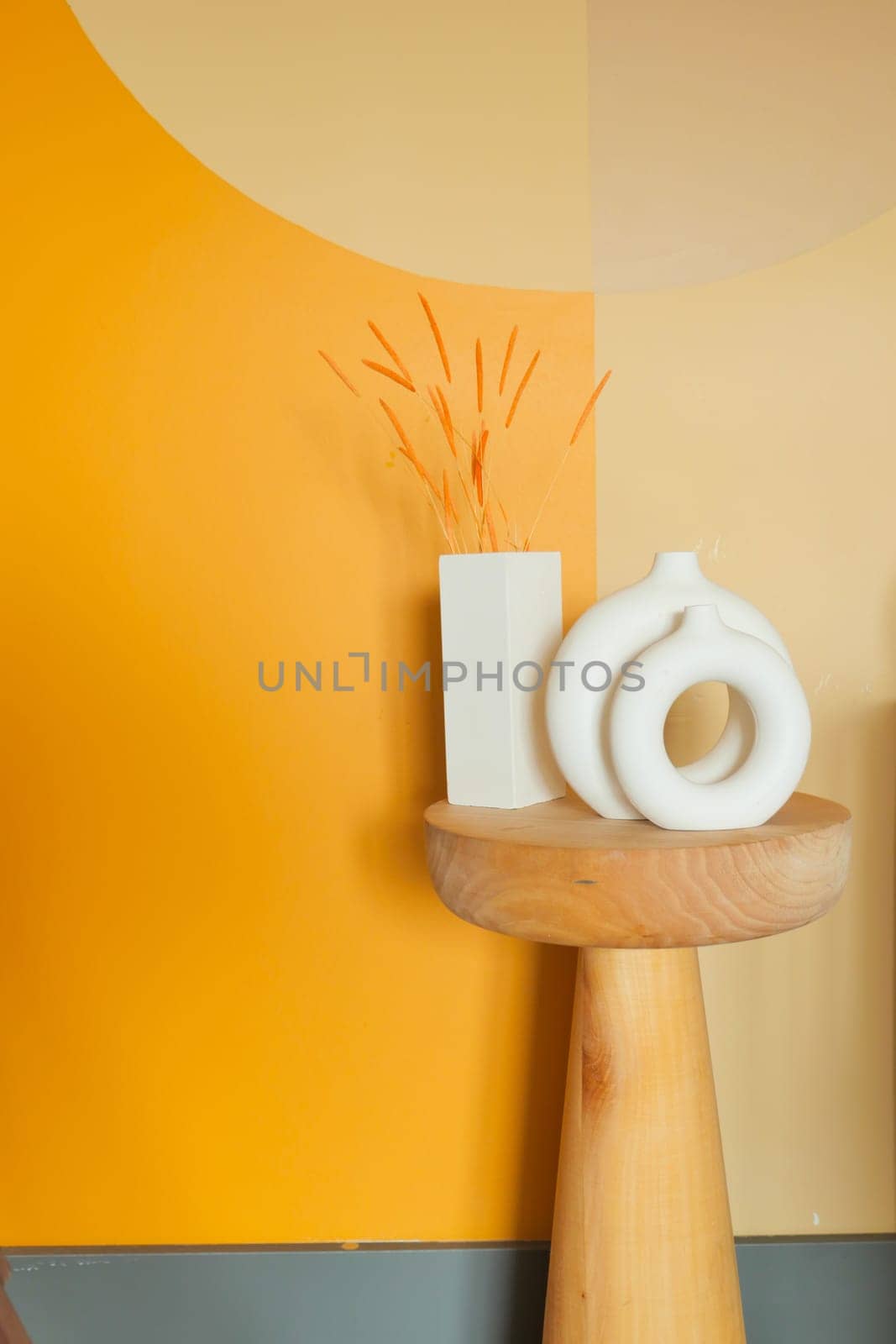 Wooden table with vase and sculpture on it, against yellow wall in room.
