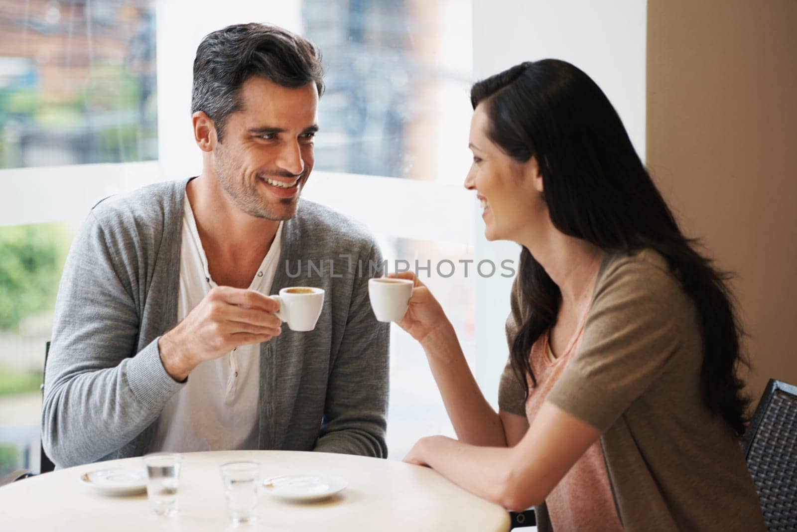 Love, conversation and couple with coffee on date for romance or anniversary in cafeteria. Happy, bonding and young man and woman talking and drinking latte, espresso or cappuccino at restaurant