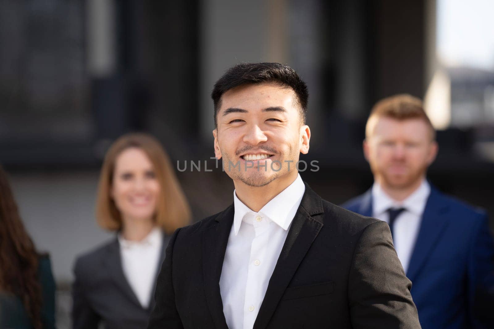 Close up portrait of smiling business asian man standing in front of his multiethnic team and looking at camera by papatonic