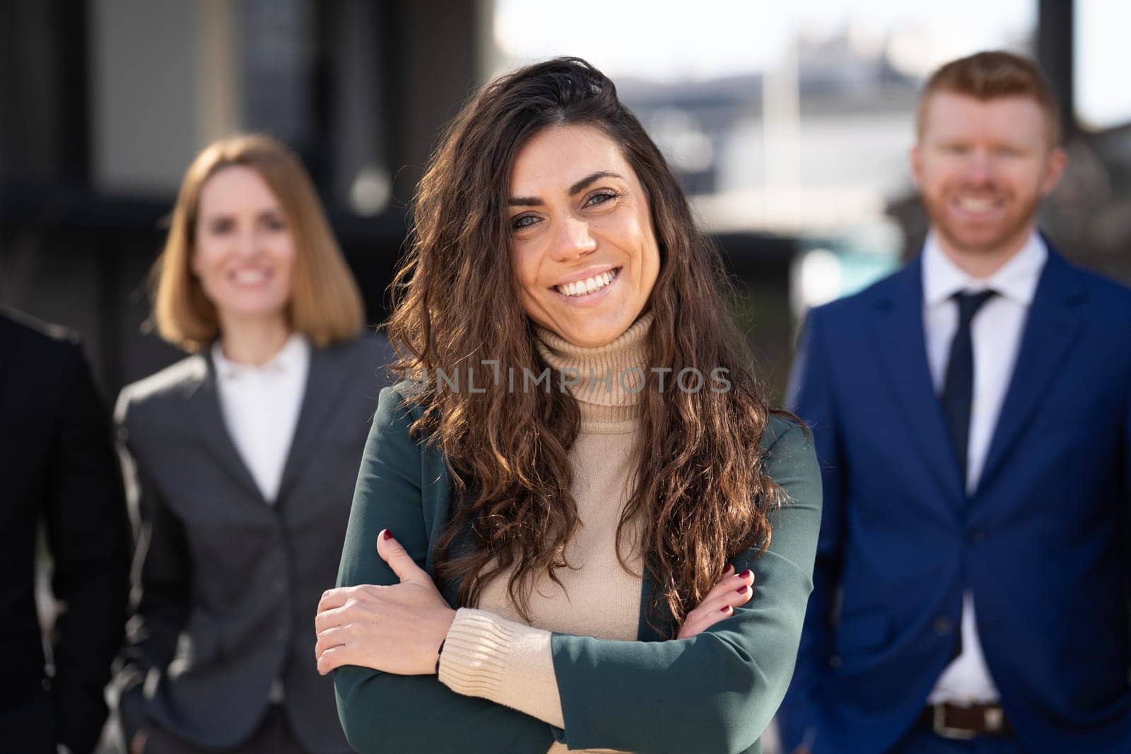Close up portrait of smiling business woman standing in front of her multiethnic team outdoors and looking at camera.