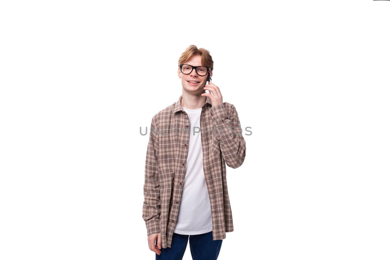 a young caucasian guy with red hair in glasses and a plaid shirt speaks on the phone.