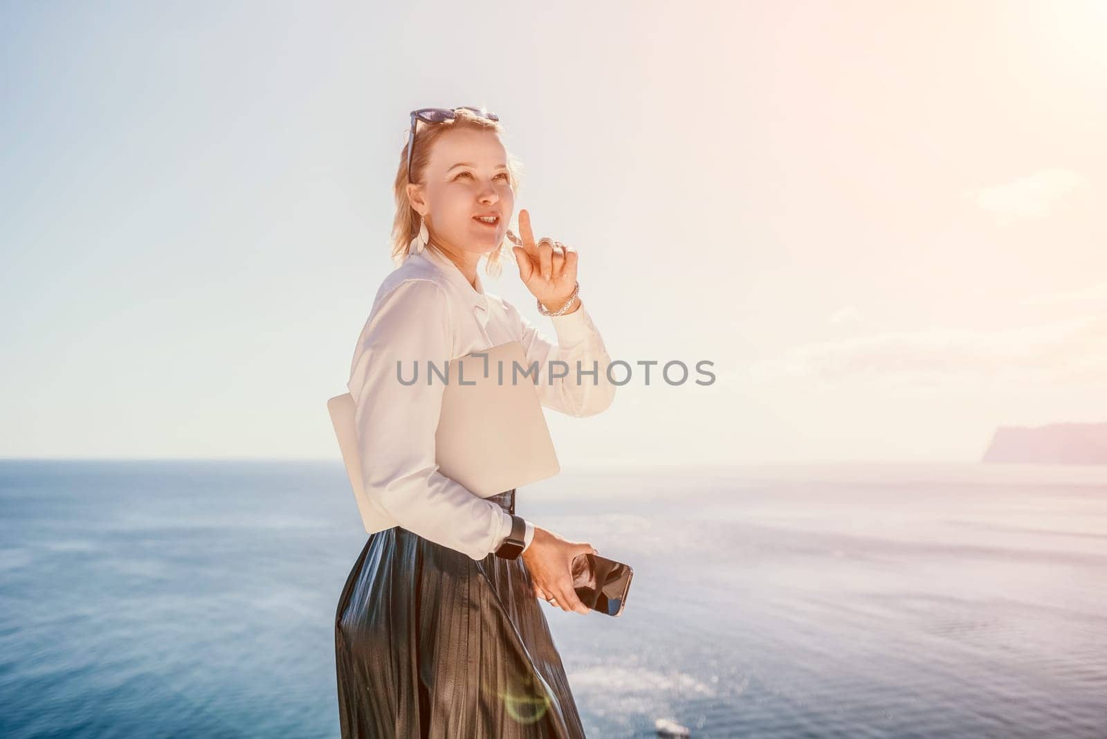 Digital nomad, Business woman working on laptop by the sea. Pretty lady typing on computer by the sea at sunset, makes a business transaction online from a distance. Freelance remote work on vacation