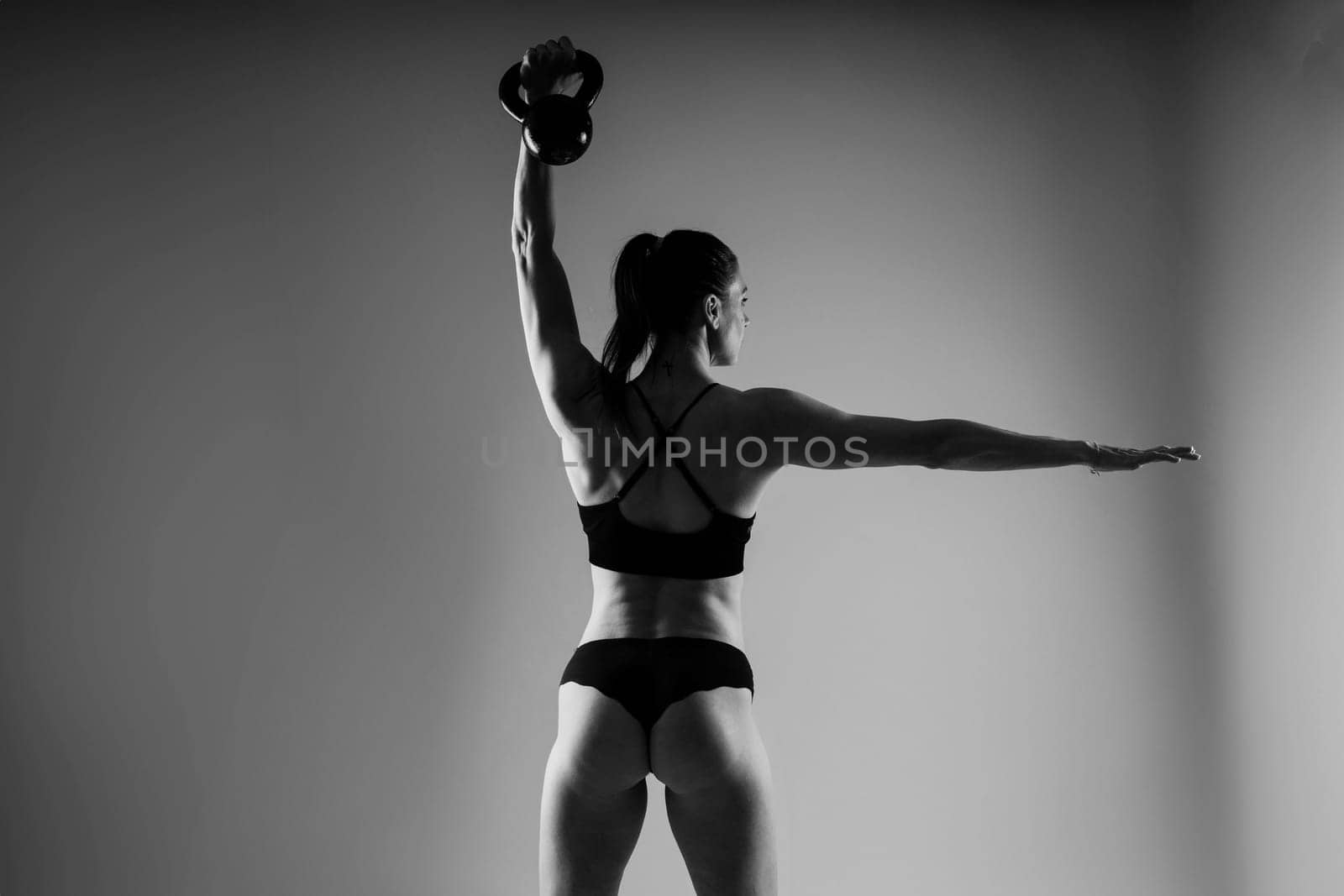 Woman in sportswear doing crossfit workout with kettle bell on dark yellow red background. by Zelenin