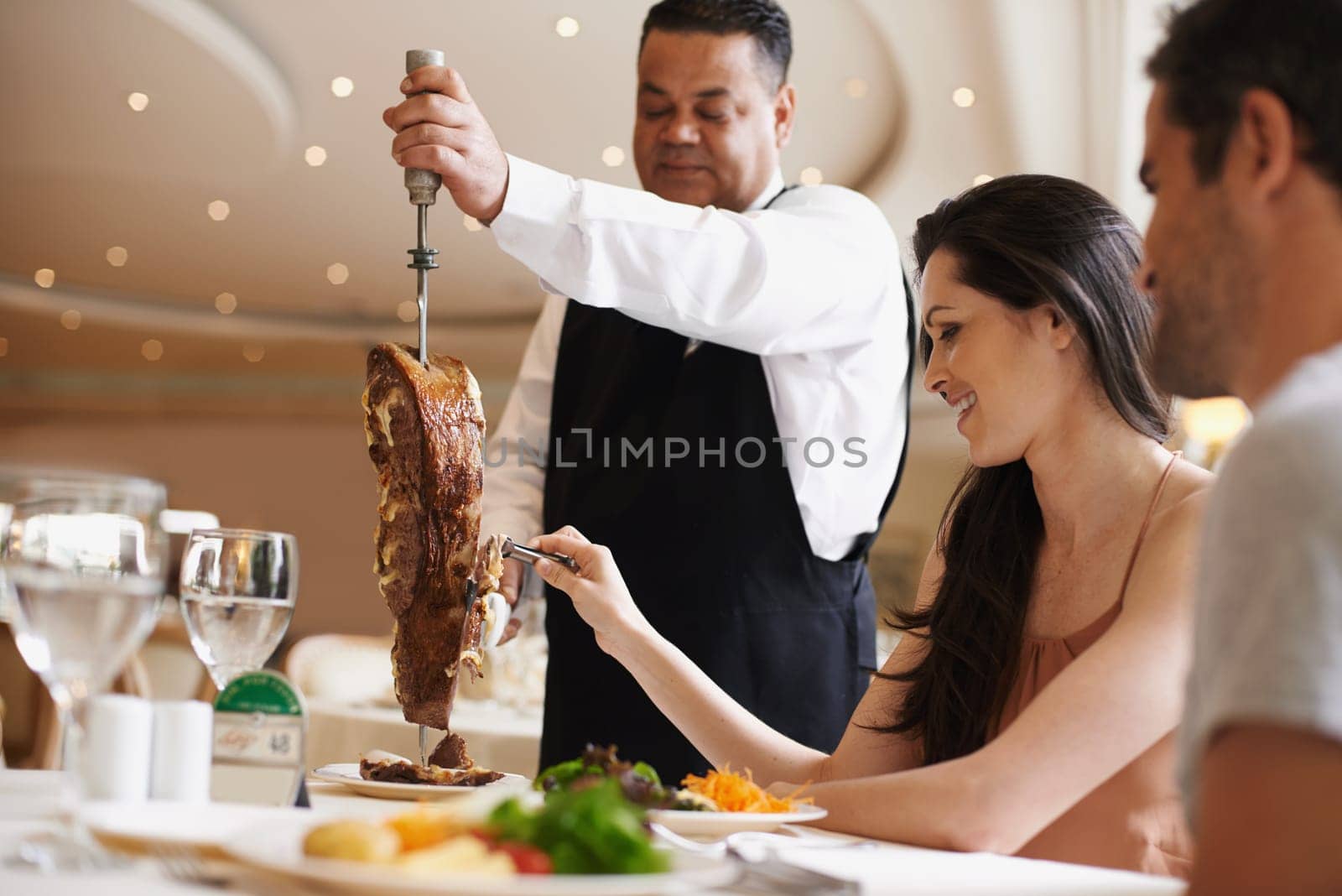 Couple, waiter and serving for dinner in restaurant with meat, happiness and fine dining for anniversary or honeymoon. Man, woman and employee with steak on skewer, healthy meal and table in London.