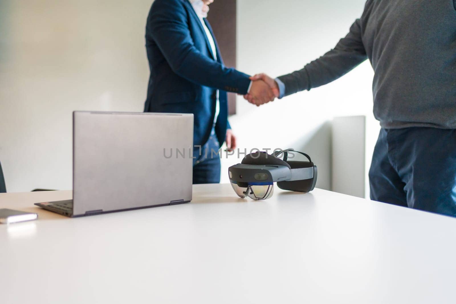 Cropped photo of a business hand shake next to laptop and augmented mixed reality goggles