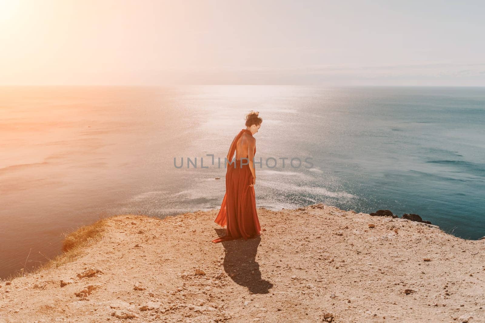 Woman red dress sea. Female dancer in a long red dress posing on a beach with rocks on sunny day. Girl on the nature on blue sky background. by Matiunina